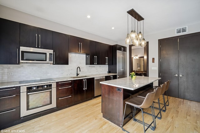 2130 W N Ave Unit 208, Chicago, IL 60647 - kitchen featuring stainless steel appliances, a sink, a breakfast bar area, backsplash, and light wood-style flooring