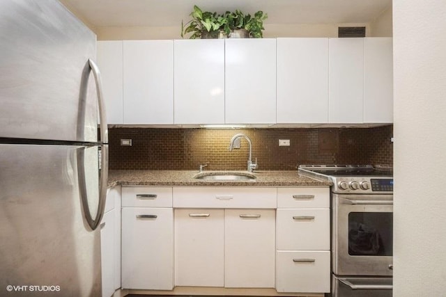 kitchen with stainless steel appliances, a sink, backsplash, light stone countertops, and white cabinetry