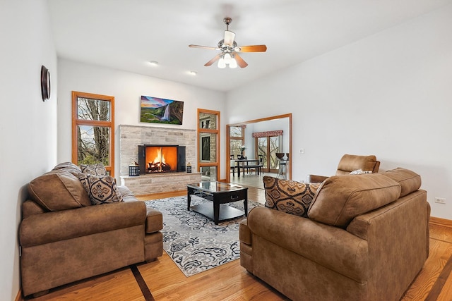 living area with light wood-style flooring, ceiling fan, and a stone fireplace