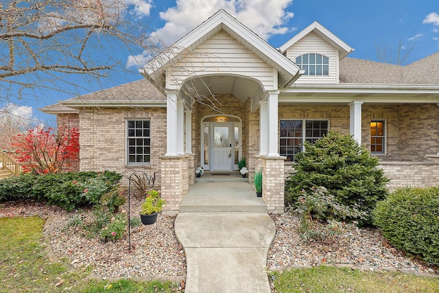view of exterior entry featuring brick siding and a shingled roof