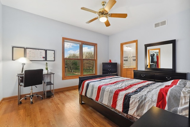 bedroom with light wood-style floors, baseboards, ensuite bath, and a ceiling fan