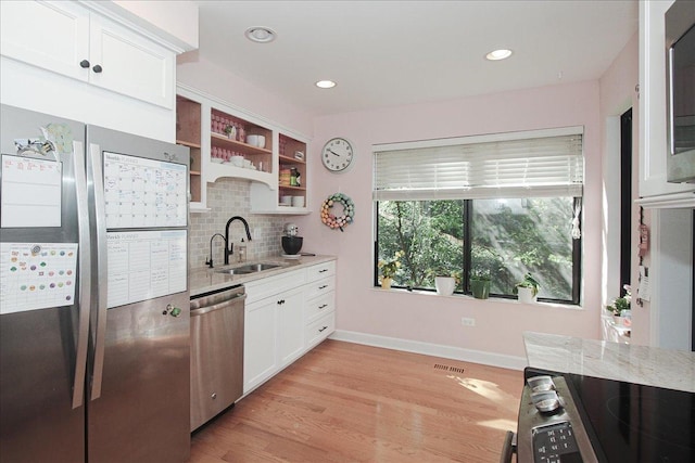 kitchen with appliances with stainless steel finishes, a sink, decorative backsplash, light stone counters, and white cabinetry