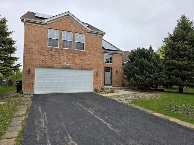 traditional-style home featuring roof mounted solar panels, an attached garage, driveway, and brick siding