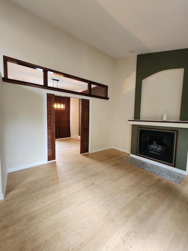 unfurnished living room featuring a fireplace, a chandelier, light wood finished floors, and baseboards