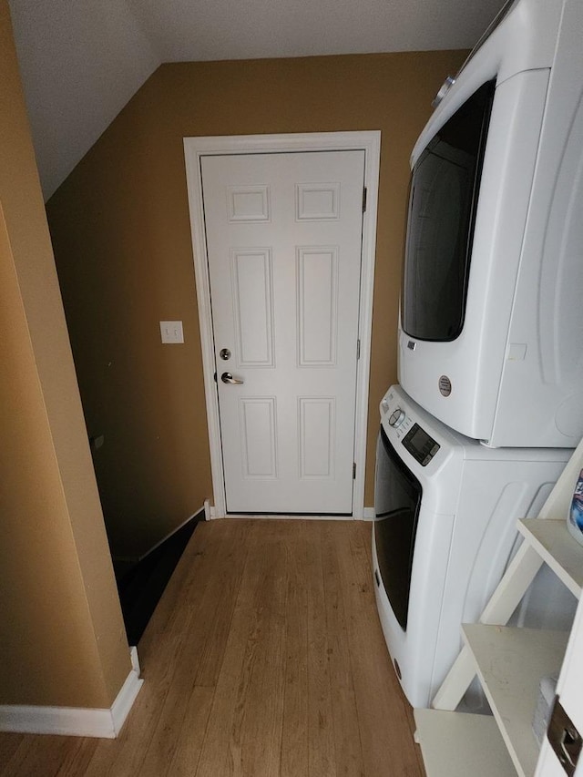 laundry room with stacked washing machine and dryer, wood finished floors, and baseboards