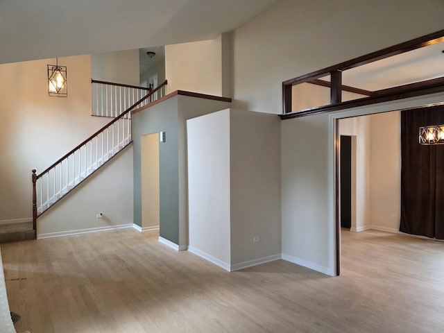 unfurnished living room with wood finished floors, a high ceiling, stairway, and baseboards