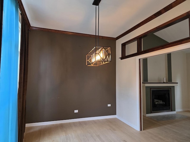 unfurnished dining area featuring light wood-style floors, a chandelier, baseboards, crown molding, and a fireplace