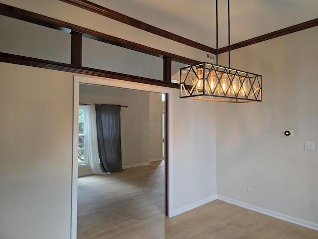 unfurnished dining area featuring light wood-type flooring, baseboards, a chandelier, and crown molding