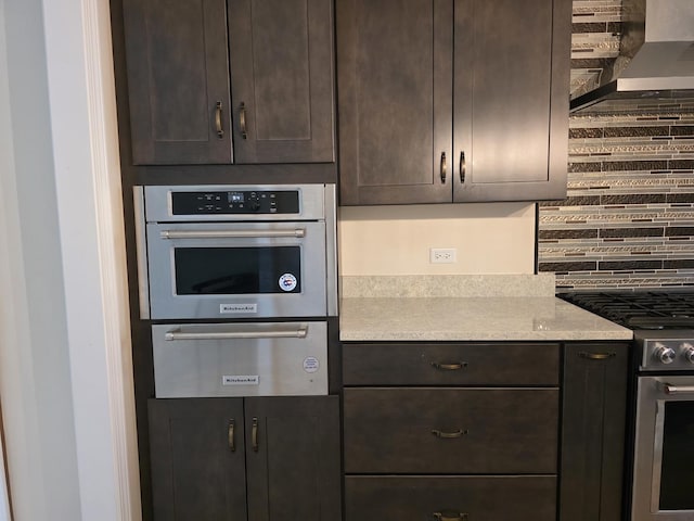 kitchen with appliances with stainless steel finishes, a warming drawer, wall chimney exhaust hood, decorative backsplash, and dark brown cabinets