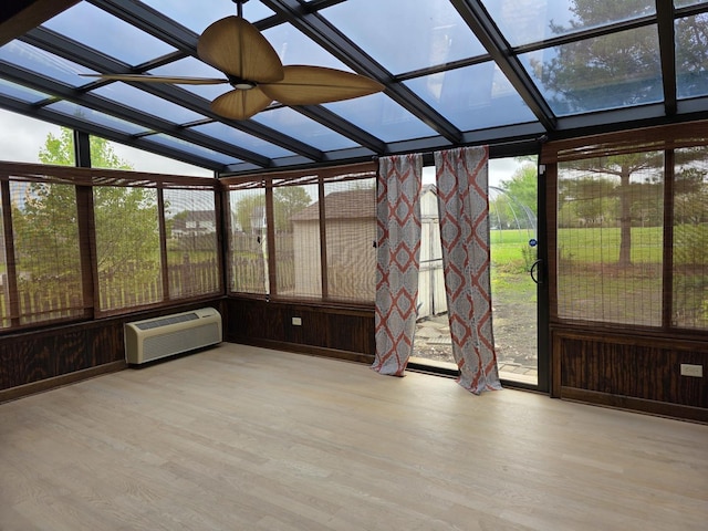 unfurnished sunroom featuring wood finished floors, a wall unit AC, a wall of windows, and vaulted ceiling