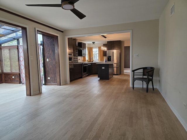 living room featuring ceiling fan, light wood finished floors, baseboards, and a chandelier