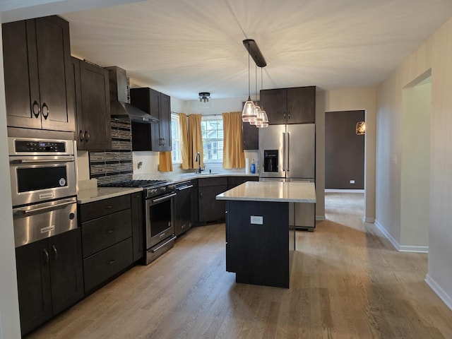 kitchen with stainless steel appliances, a warming drawer, wall chimney exhaust hood, light wood finished floors, and a center island