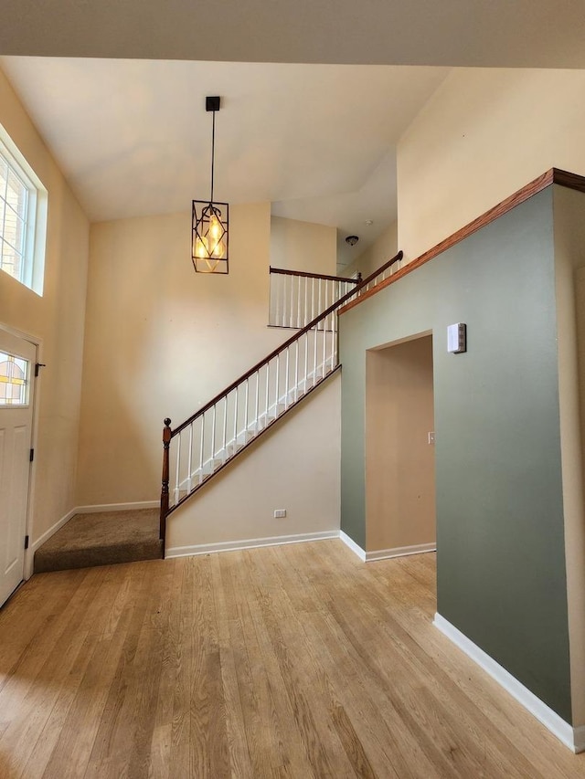 entryway with light wood-type flooring, baseboards, stairway, and high vaulted ceiling