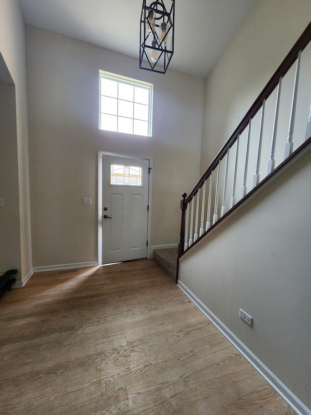 foyer entrance with stairs, baseboards, wood finished floors, a high ceiling, and a chandelier