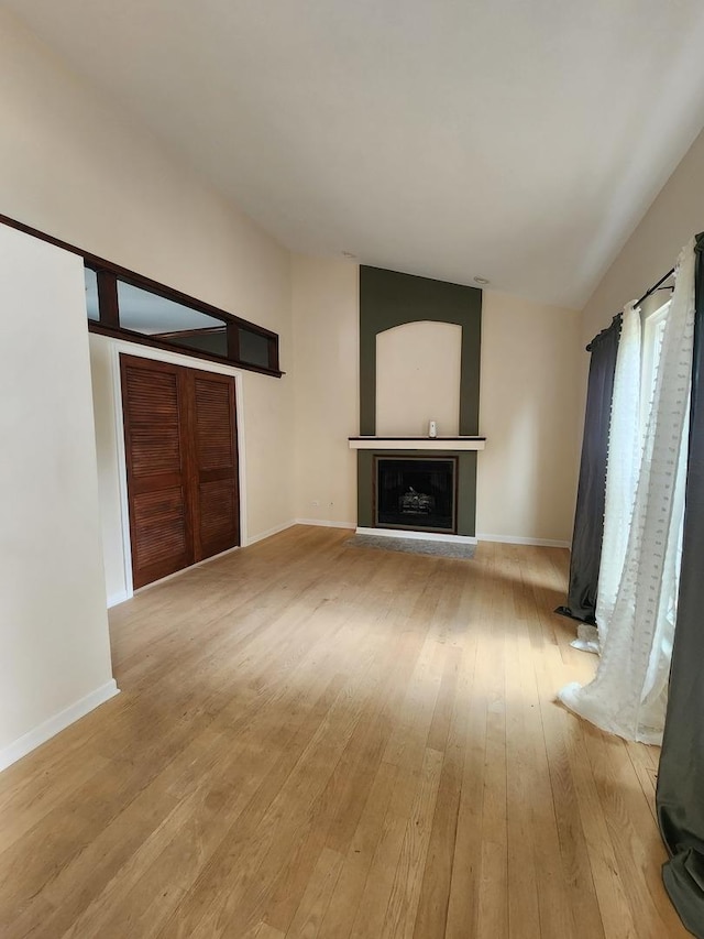 unfurnished living room with light wood-style flooring, a fireplace with raised hearth, and baseboards