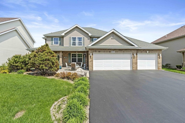 view of front of property with asphalt driveway, an attached garage, a front yard, covered porch, and brick siding