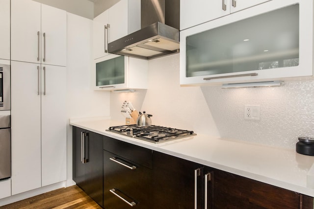 kitchen featuring wall chimney exhaust hood, light countertops, white cabinets, dark wood-style flooring, and glass insert cabinets