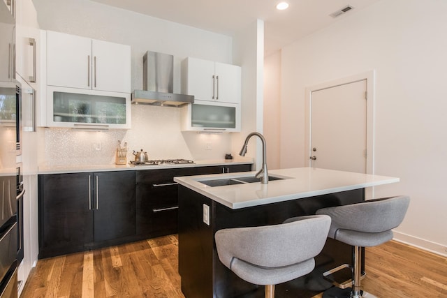 kitchen with wall chimney exhaust hood, a sink, a breakfast bar, light wood-style flooring, and recessed lighting