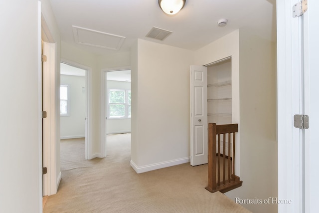 hallway featuring light carpet, an upstairs landing, attic access, and baseboards