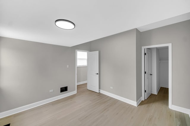 unfurnished bedroom featuring light wood-style flooring, baseboards, a walk in closet, and a closet