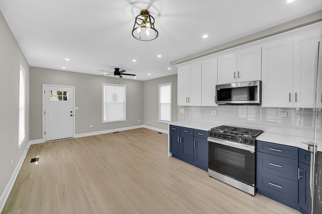 kitchen with stainless steel appliances, white cabinetry, blue cabinets, light countertops, and baseboards