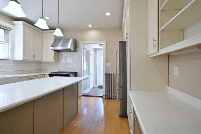 5813 W Eastwood Ave, Chicago, IL 60630 - kitchen featuring wall chimney exhaust hood, radiator, appliances with stainless steel finishes, tasteful backsplash, and light wood-type flooring