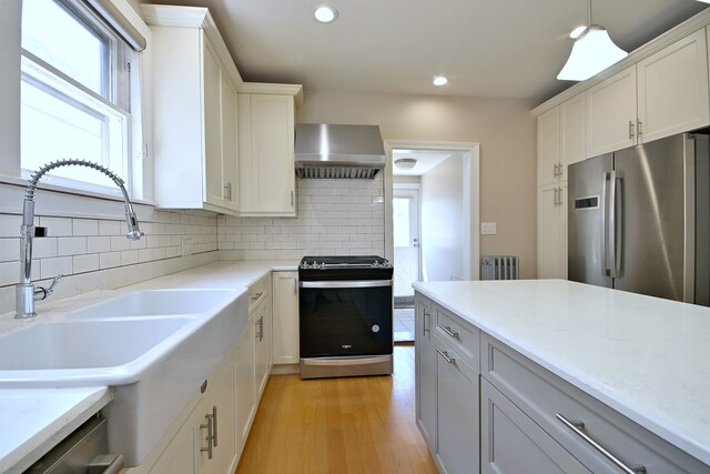 5813 W Eastwood Ave, Chicago, IL 60630 - kitchen featuring appliances with stainless steel finishes, radiator, a sink, wall chimney range hood, and plenty of natural light
