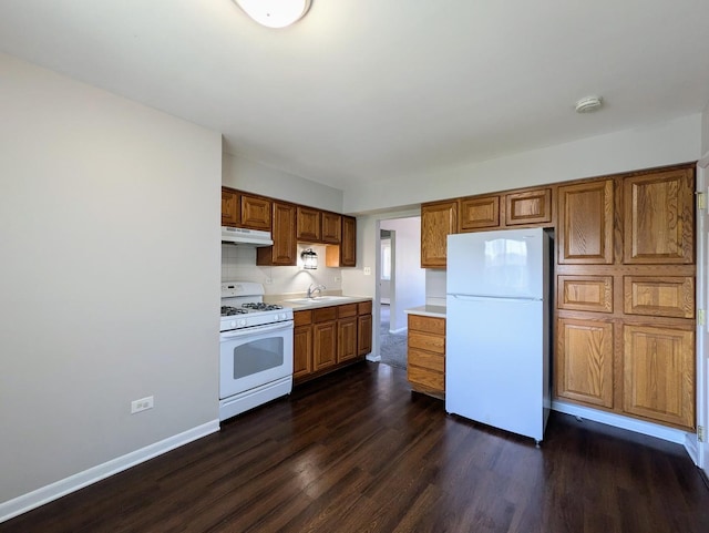 kitchen with white appliances, under cabinet range hood, dark wood-type flooring, brown cabinets, and light countertops