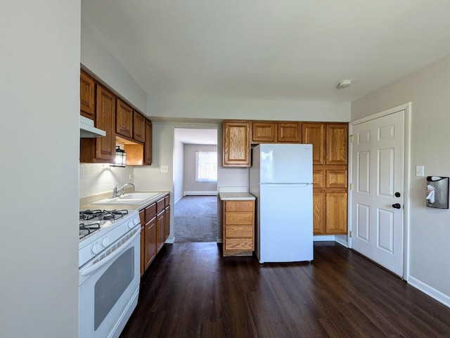 kitchen with white appliances, a sink, dark wood-style flooring, and brown cabinets