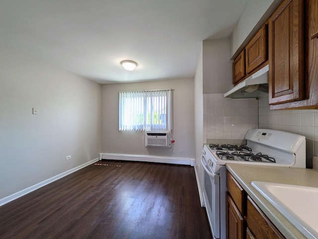 kitchen with white gas range, under cabinet range hood, dark wood finished floors, brown cabinets, and tasteful backsplash