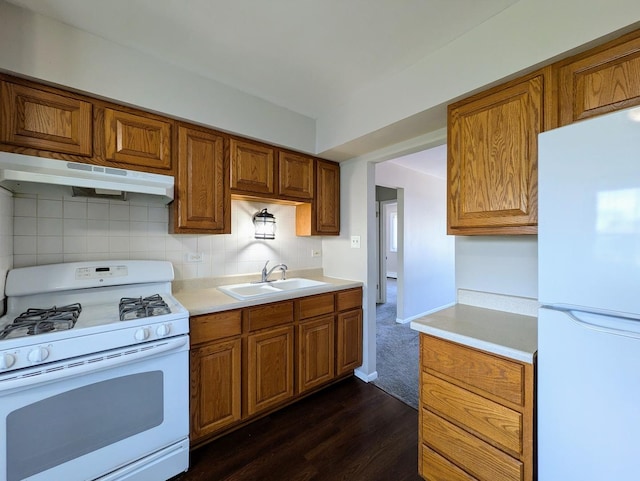 kitchen with white appliances, under cabinet range hood, a sink, brown cabinetry, and light countertops