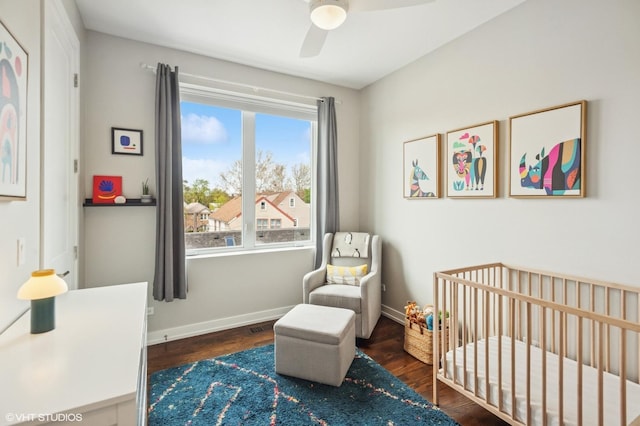 bedroom with wood finished floors, a crib, baseboards, and a ceiling fan