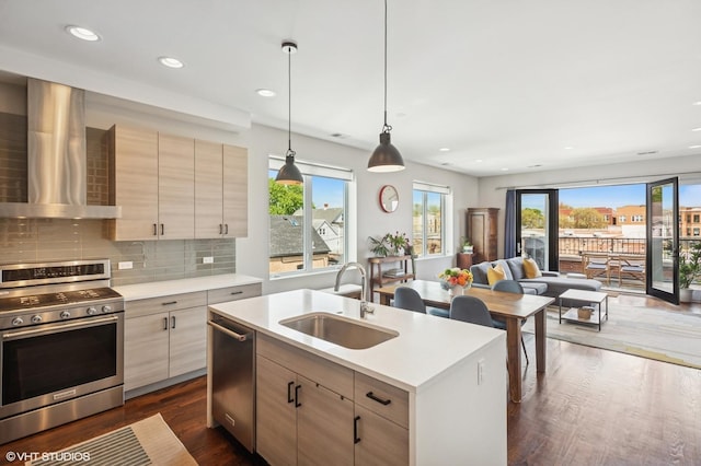 kitchen featuring stainless steel appliances, a sink, wall chimney exhaust hood, open floor plan, and light countertops