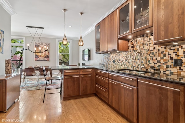 kitchen with a sink, healthy amount of natural light, light wood finished floors, decorative backsplash, and crown molding