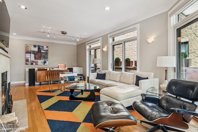 living room featuring ornamental molding, wood finished floors, a glass covered fireplace, recessed lighting, and baseboards