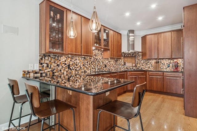 bar area with a sink, wall chimney range hood, light wood-type flooring, backsplash, and pendant lighting