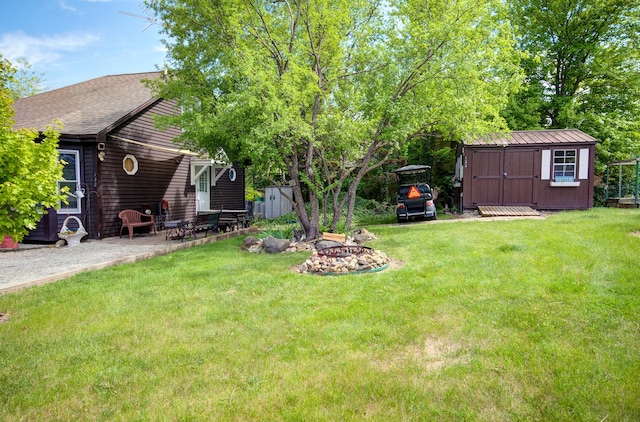 view of grassy yard featuring a shed, an outdoor fire pit, an outbuilding, and a patio