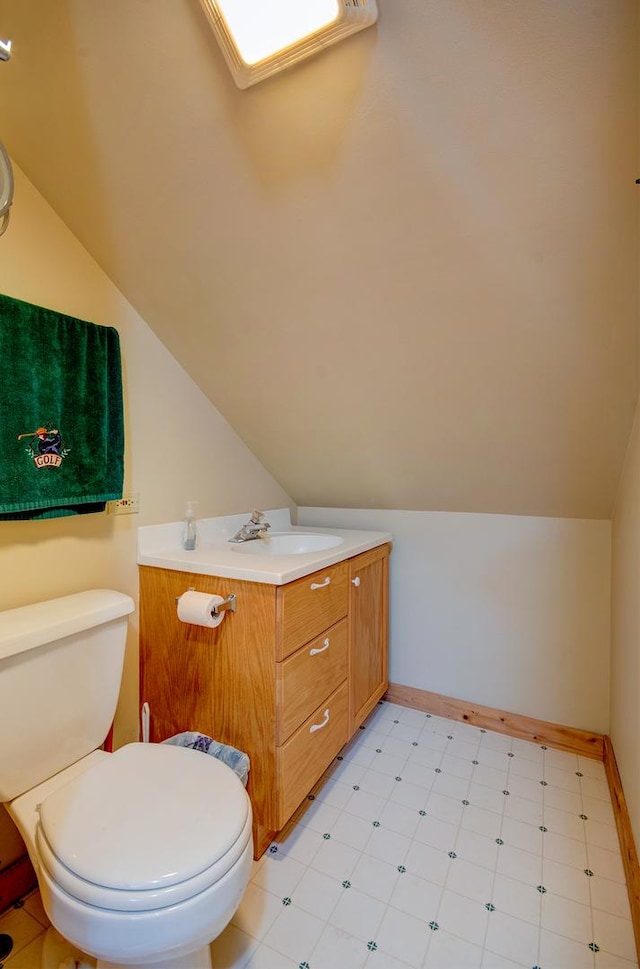 half bathroom with tile patterned floors, vaulted ceiling, toilet, vanity, and baseboards