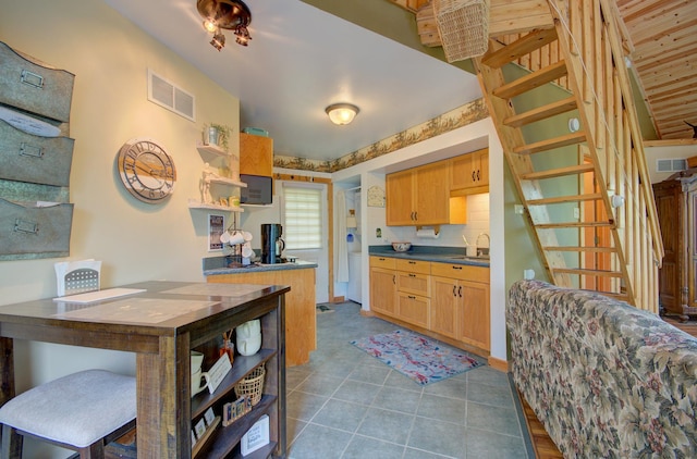 kitchen with a sink, dark countertops, dark tile patterned flooring, light brown cabinets, and open shelves