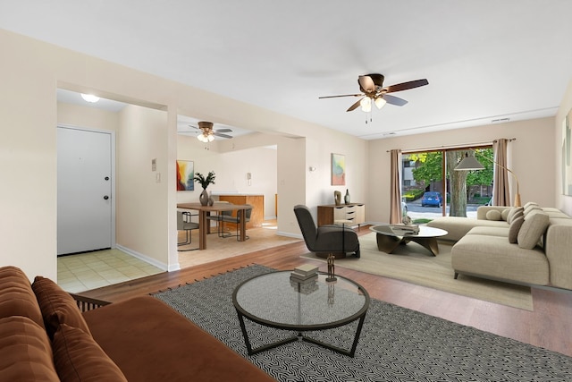 living area featuring a ceiling fan, light wood finished floors, and baseboards