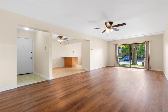 unfurnished living room featuring a ceiling fan, wood finished floors, and baseboards