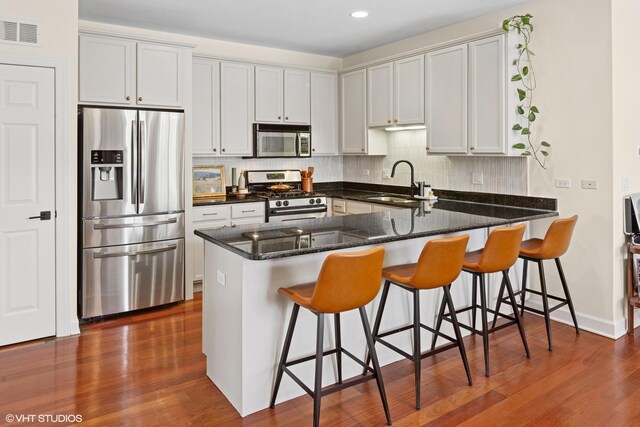 kitchen with stainless steel appliances, a sink, a peninsula, dark stone countertops, and backsplash