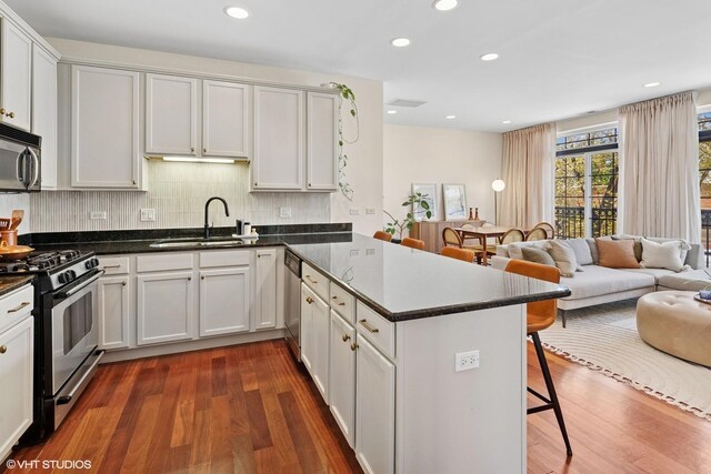 kitchen with stainless steel appliances, a sink, open floor plan, a peninsula, and dark wood-type flooring