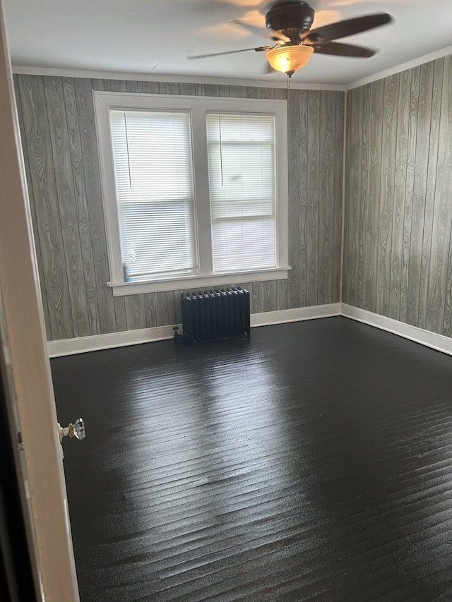 720 S Carroll Ave, Freeport, IL 61032 - empty room featuring radiator heating unit, baseboards, ceiling fan, wood finished floors, and wood walls