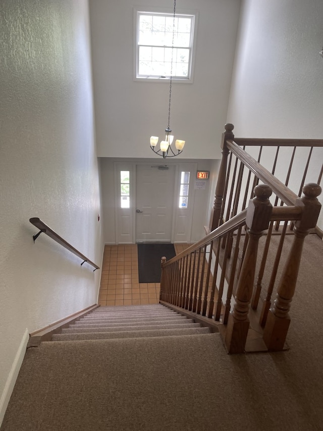 stairs with a towering ceiling, carpet floors, a chandelier, a textured wall, and baseboards
