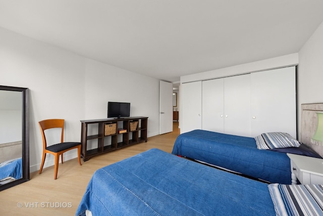 bedroom with light wood-style flooring, baseboards, and a closet