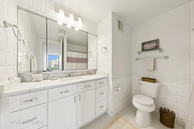 bathroom with tile walls, toilet, vanity, tile patterned flooring, and wainscoting