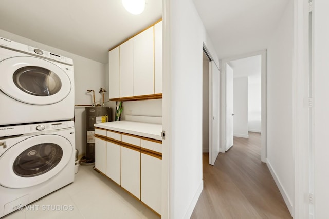 laundry area featuring stacked washing machine and dryer, electric water heater, cabinet space, light wood finished floors, and baseboards