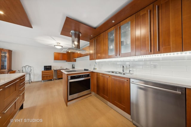 kitchen featuring appliances with stainless steel finishes, island range hood, a sink, light wood-style floors, and brown cabinetry