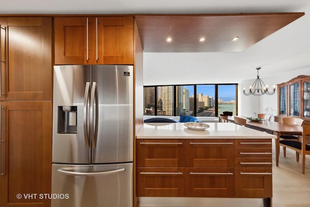 kitchen with stainless steel fridge with ice dispenser, brown cabinets, a chandelier, light countertops, and a peninsula